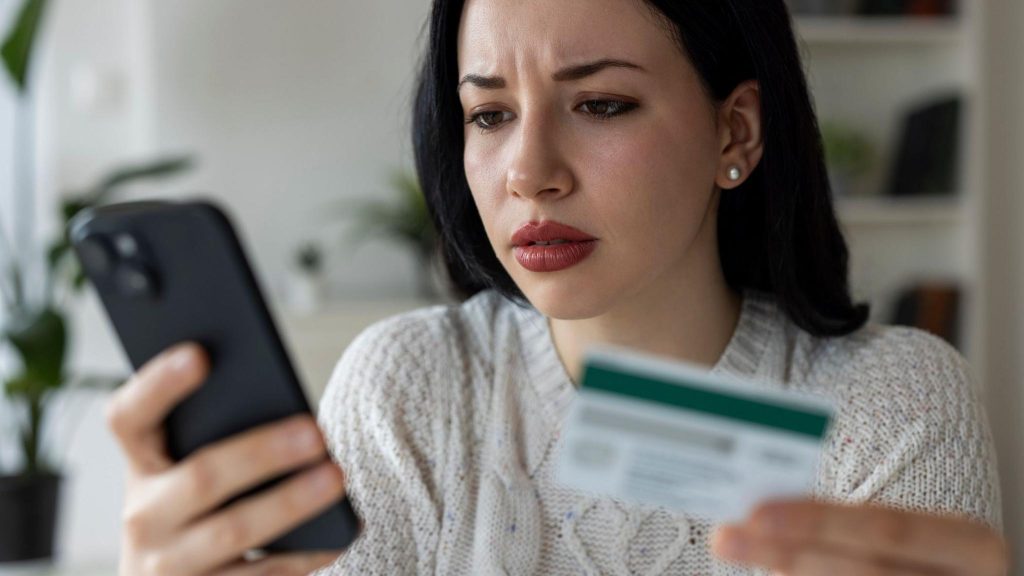 Woman with dark hair holds a credit card in one hand and a smartphone in the other.