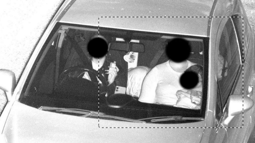 Two women sit in a car, with the passenger holding a small child. All of their faces are blacked out.