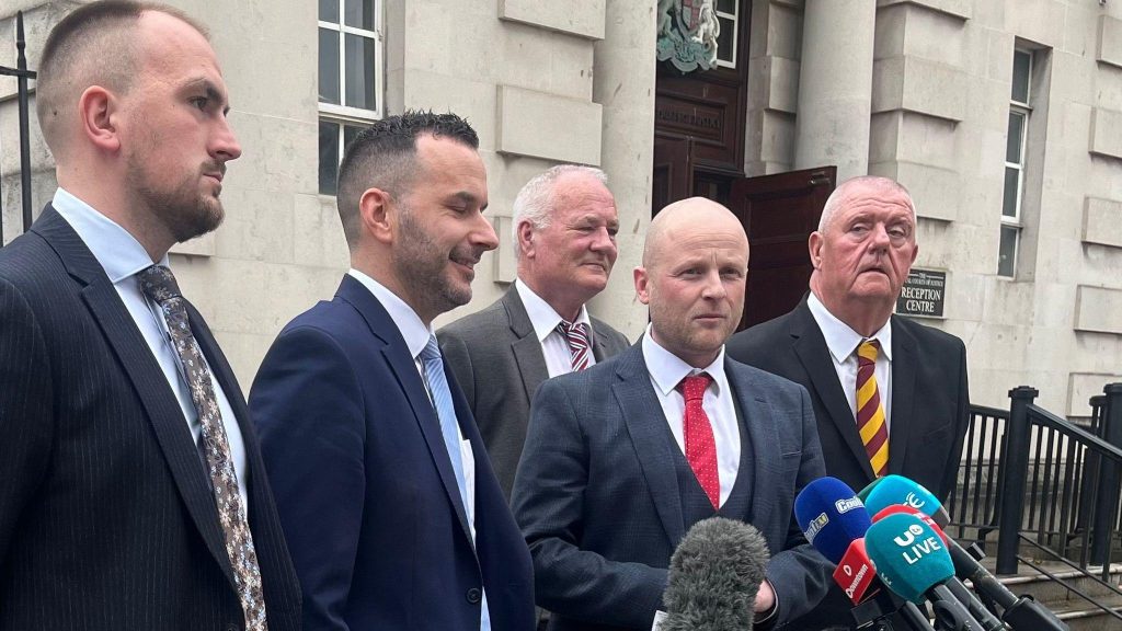 Five men wearing suits in different colours talking into mics outside court.