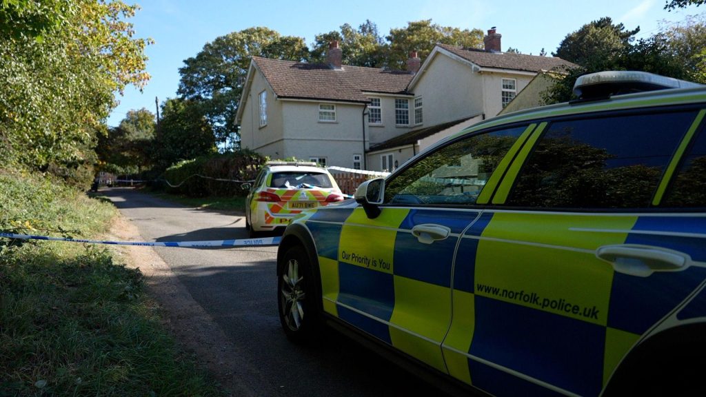Two police cars outside a large property on a lane in a village.