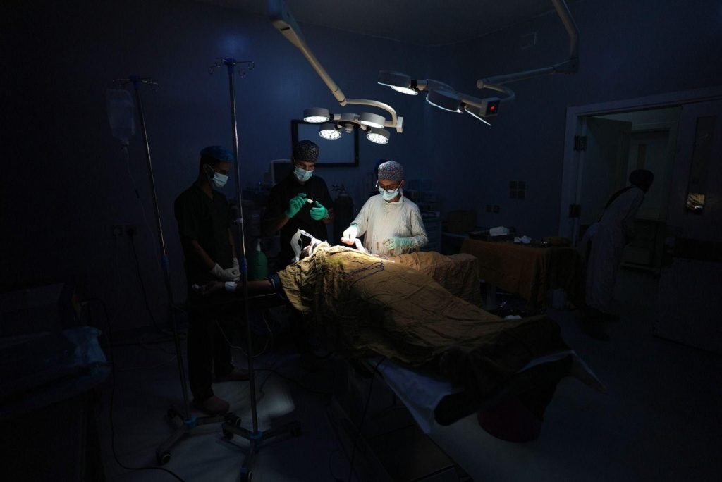Medics surround a patient in an operating theatre in a military hospital lit only by portable lights