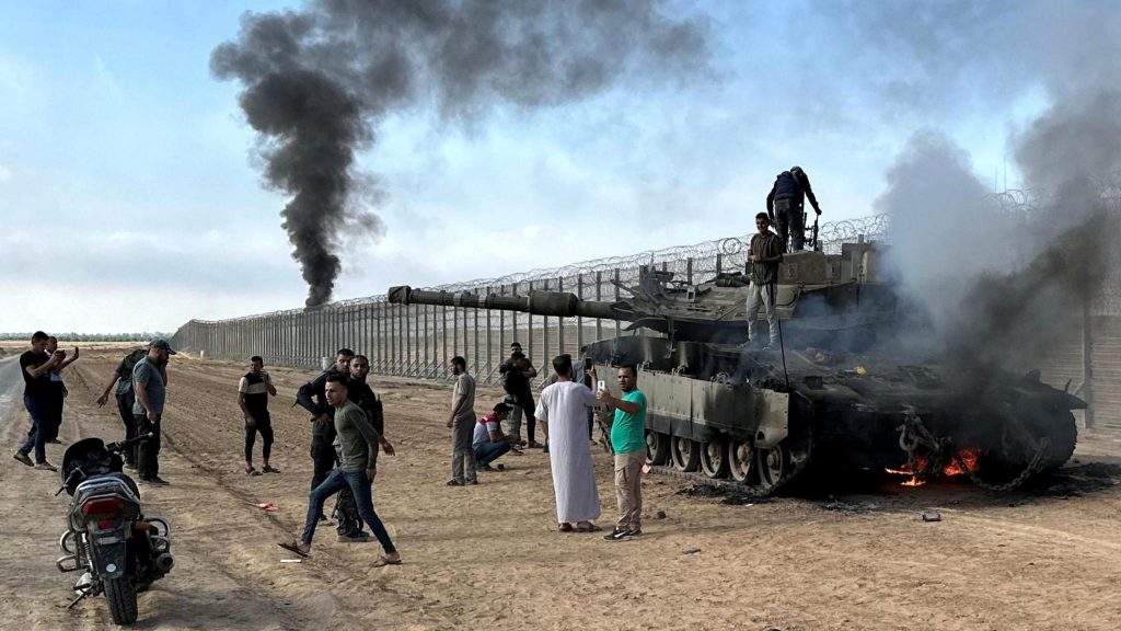 File photo showing Palestinians gathered around an Israeli tank set on fire during the Hamas-led 7 October 2023 attack on Israel, on the Israeli side of the Gaza border fence